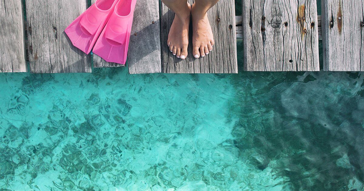 Bare feet and pink swim fins on a dock above clear turquoise water