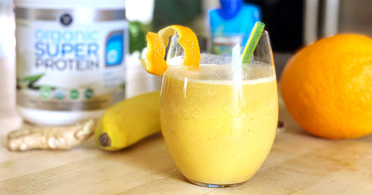 Orange smoothie beside Organic Super Protein, a banana, ginger and an orange