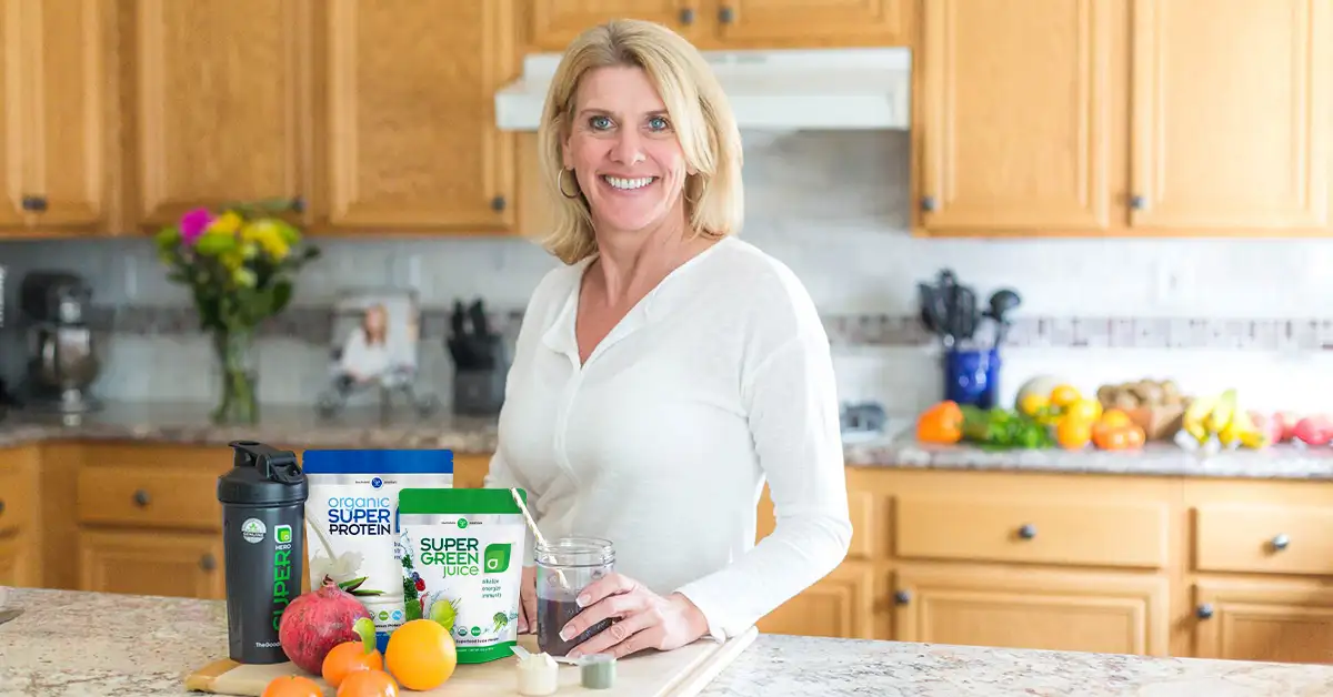 Smiling woman in a kitchen with Organic Super Protein, Super Green Juice and fresh fruit